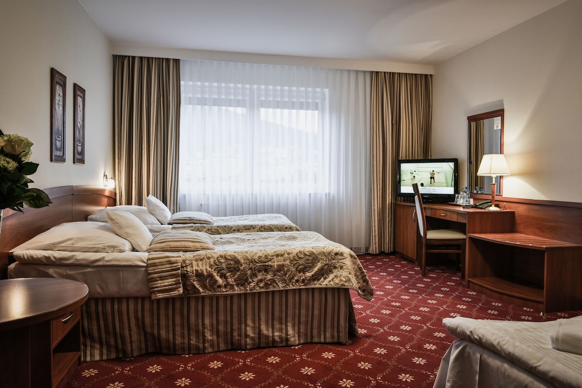 A hotel room with two beds, a desk, a TV, and a chair.