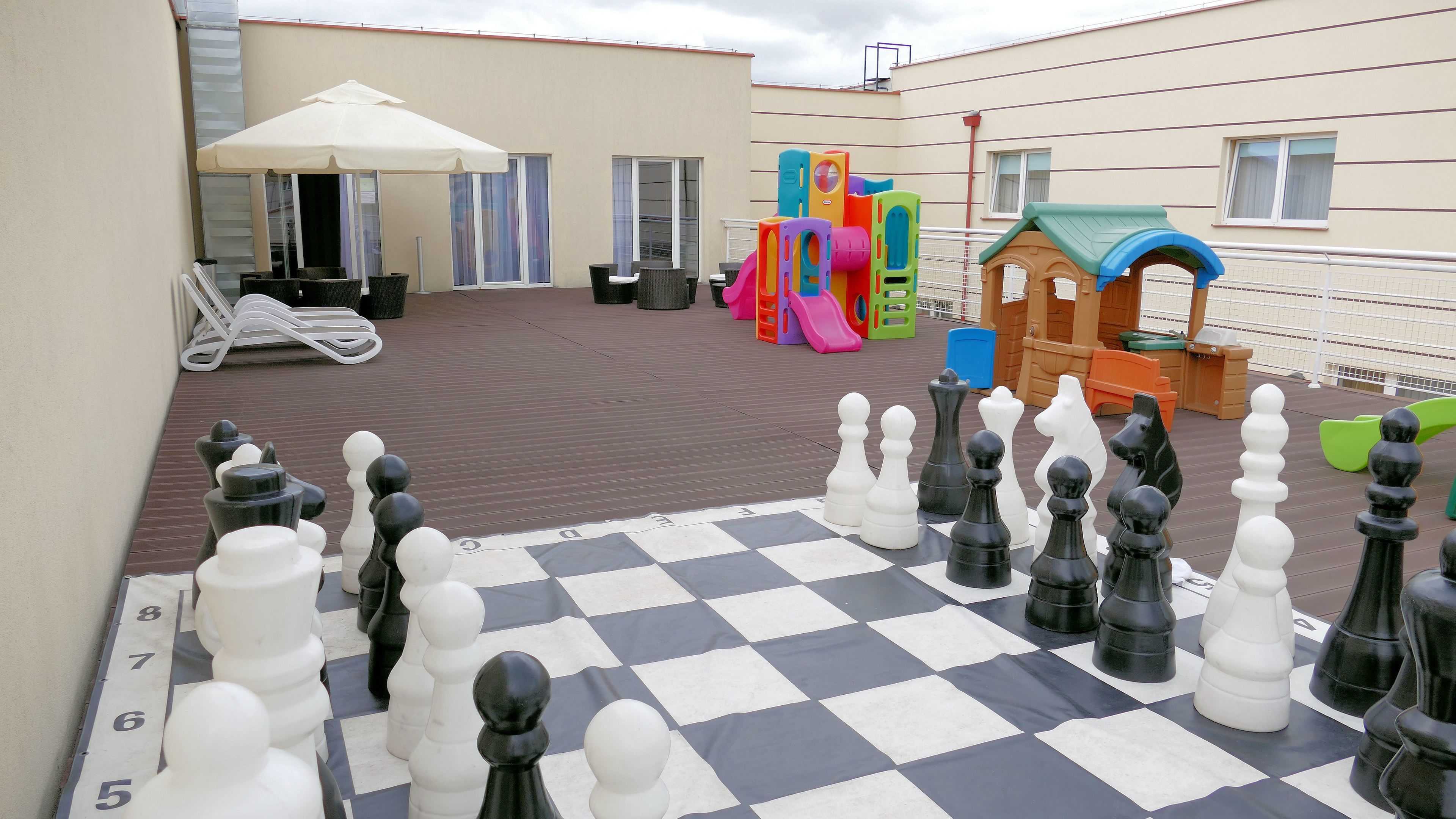 A checkered chessboard with chess pieces, outdoor seating, and children's play equipment.
