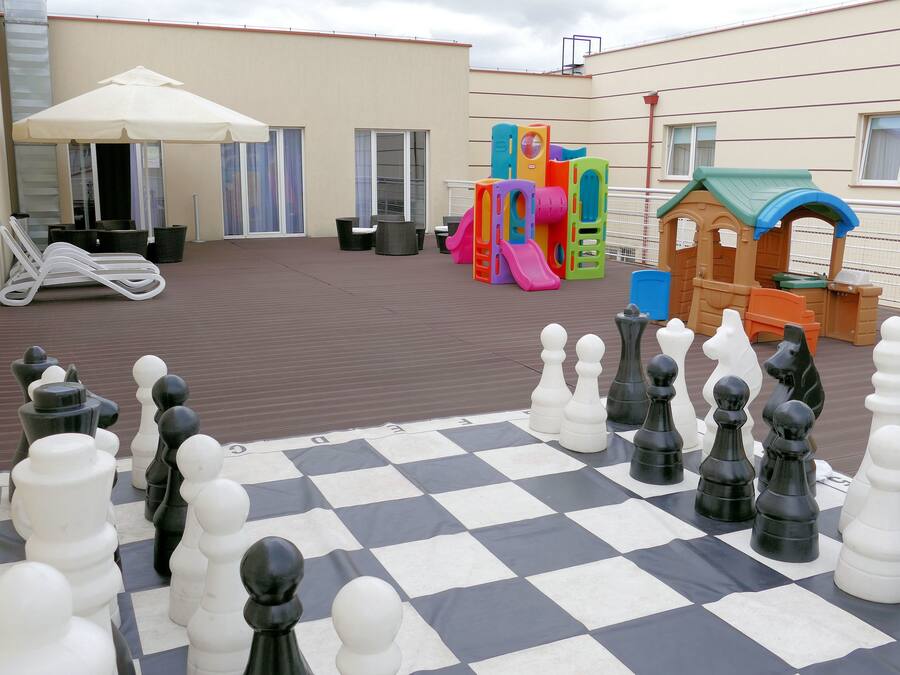 A checkered chessboard with chess pieces, outdoor seating, and children's play equipment.