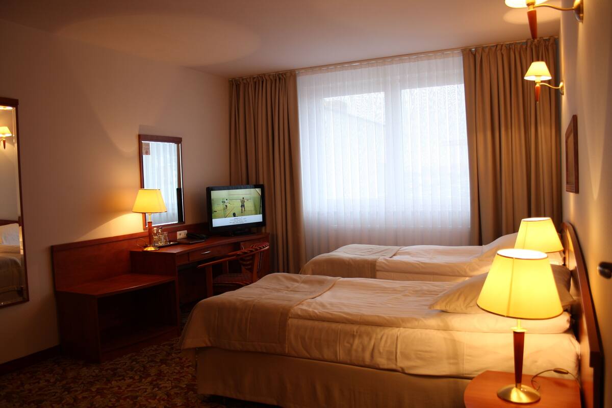 A hotel room with two beds, a desk with a television, and lamps.