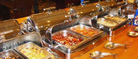 A buffet with various food items in metal containers, arranged on a wooden table.