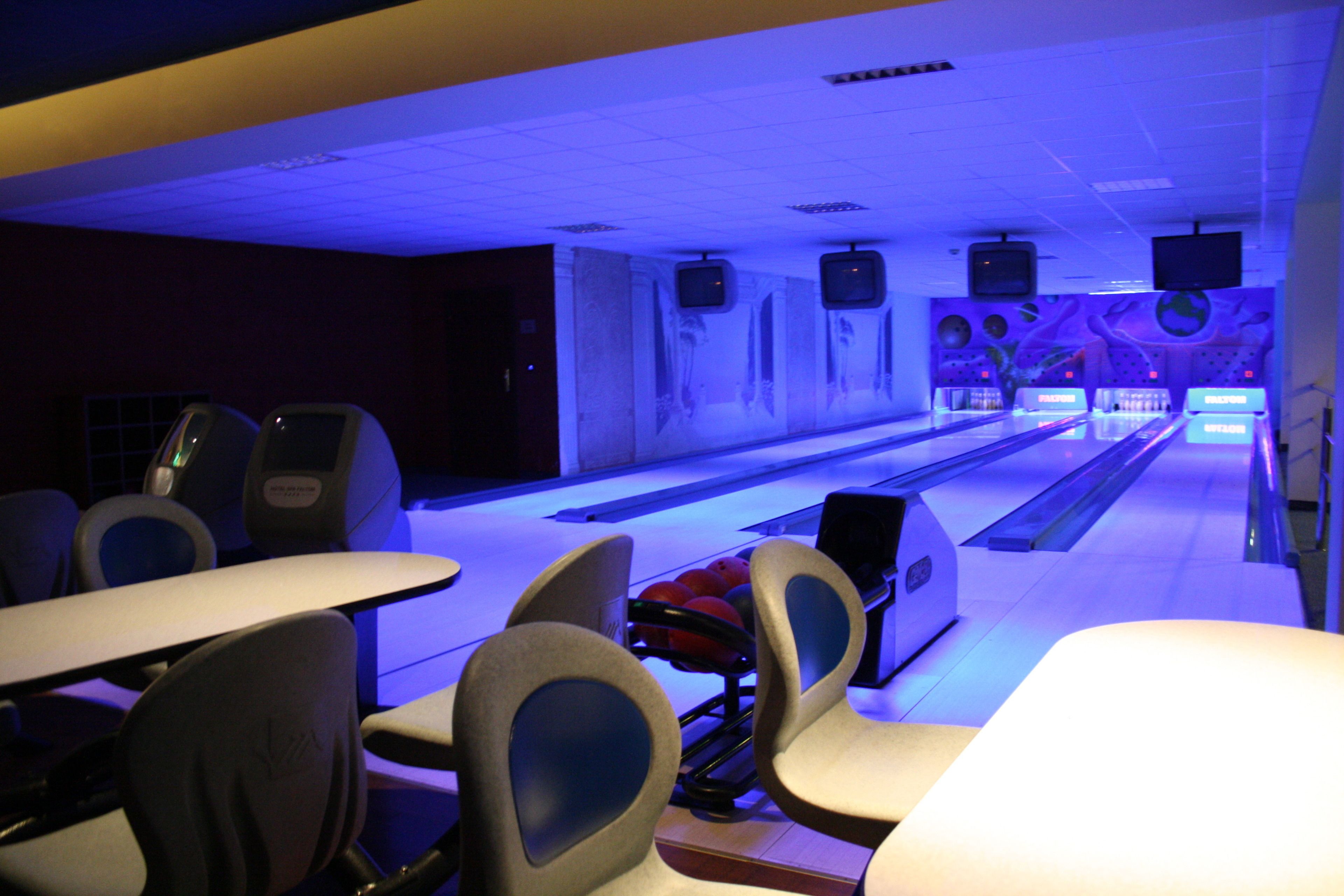 A bowling alley with multiple lanes, seating areas, and overhead televisions.