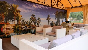 Una habitación con un mural tropical, muebles de mimbre blanco y vistas al exterior.