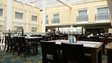 A spacious indoor dining area with multiple tables and chairs, large windows, and a high ceiling with a skylight.