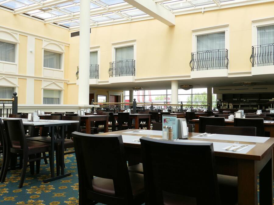 A spacious indoor dining area with multiple tables and chairs, large windows, and a high ceiling with a skylight.