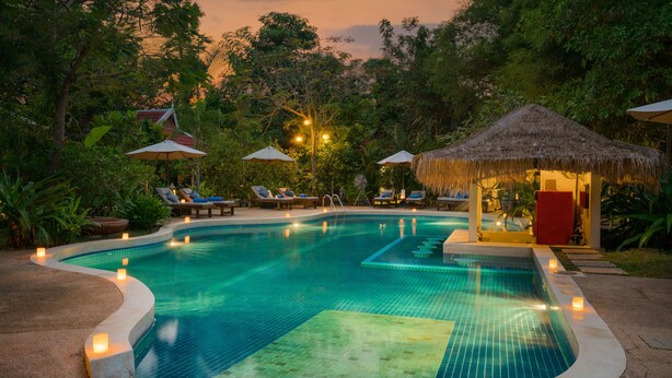 Una piscina con sillones de descanso y sombrillas, rodeada de abundante vegetación.