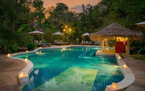 A swimming pool with lounge chairs and umbrellas, surrounded by lush greenery. - Sojourn Boutique Villas (Siem Reap)