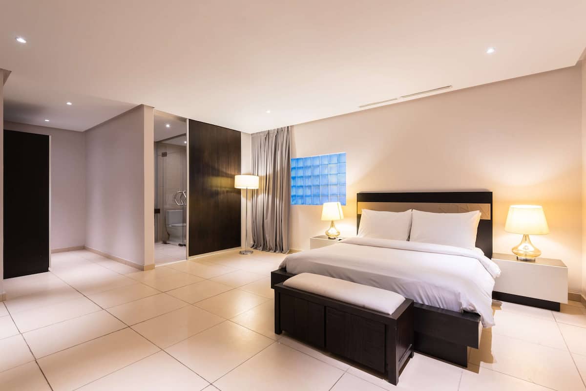Ein modernes Hotelzimmer mit einem großen Bett, Nachttischen und einem durch eine geöffnete Tür einsehbaren Badezimmer.