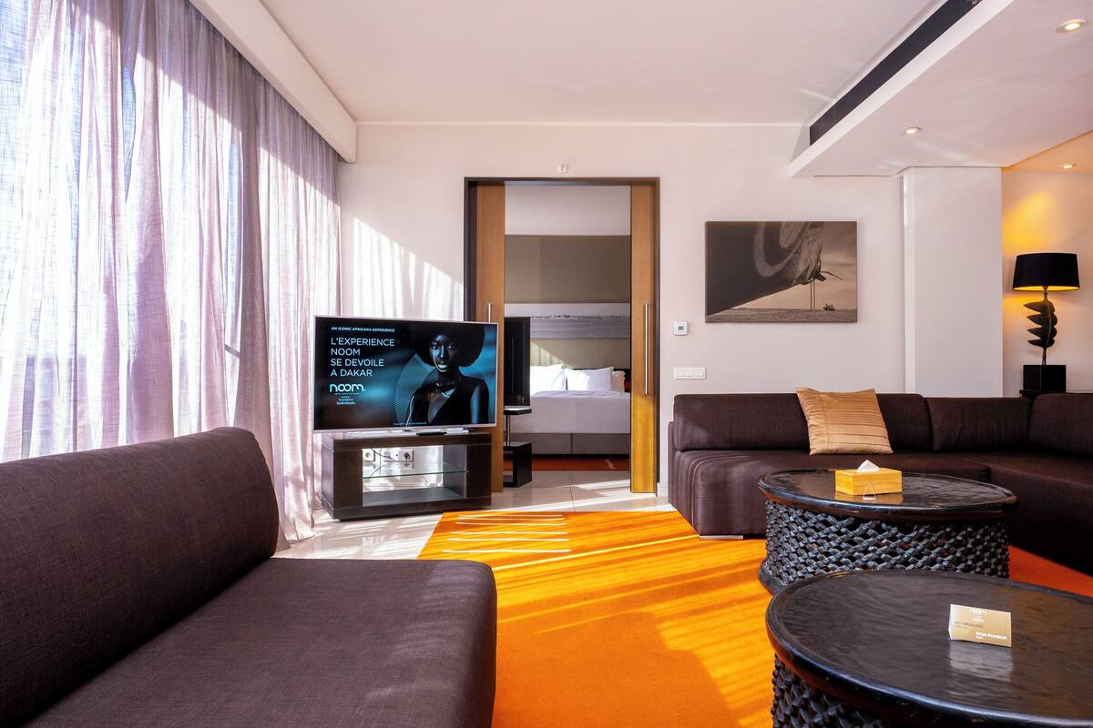 Ein modernes Hotelzimmer mit großem Flachbildfernseher, einer Couch, einem Couchtisch und einem gemusterten Teppich.