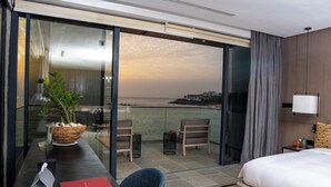 Un cuarto de hotel con una cama, un escritorio con una computadora portátil, una silla, una mesita con una planta y vistas al mar.
