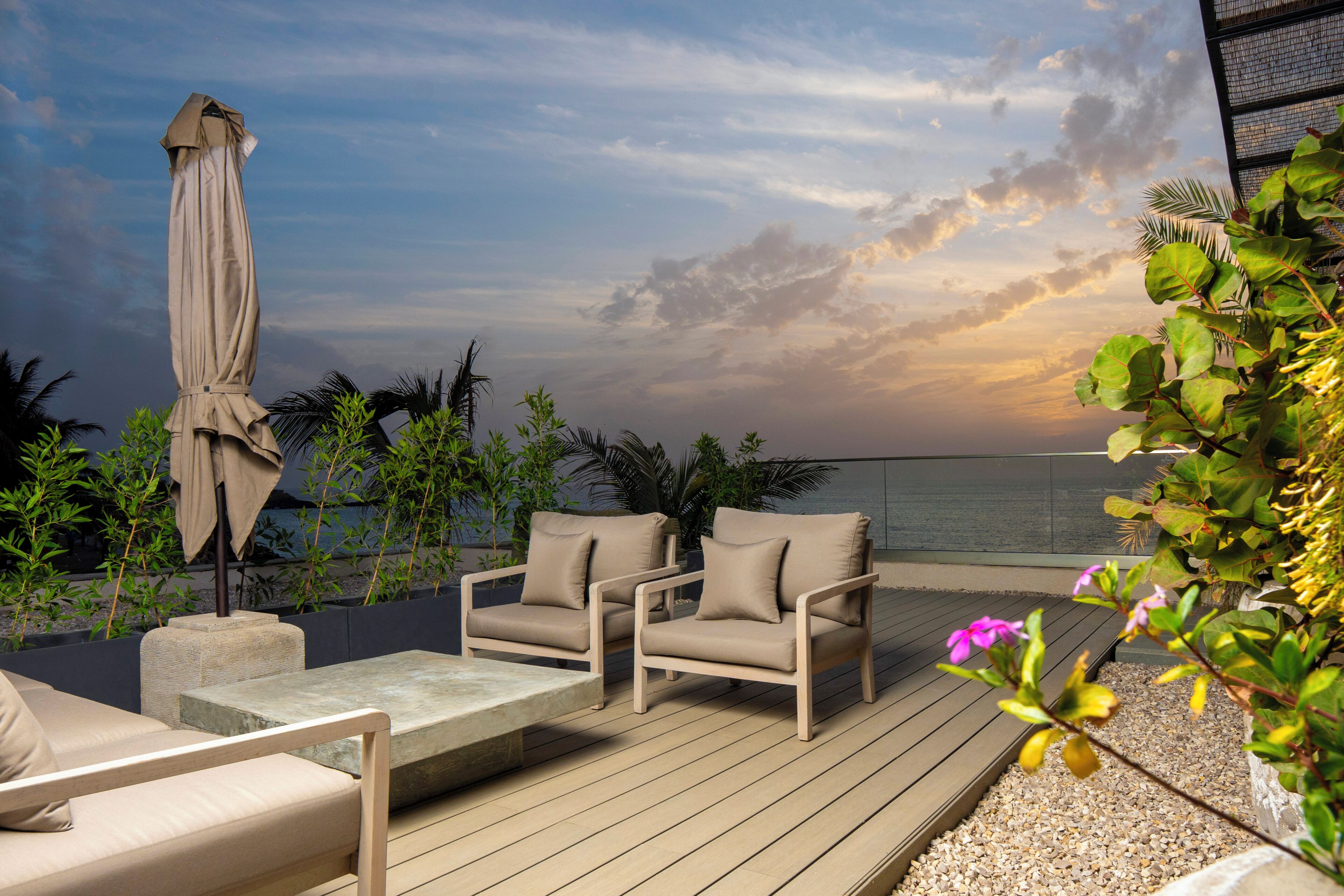 A deck with two beige chairs, a table, and an umbrella.