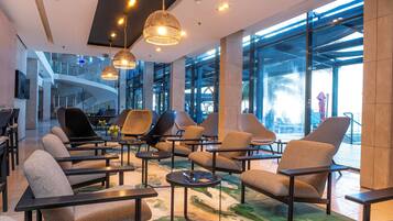 A spacious lobby with modern seating, large windows, and a staircase in the background.