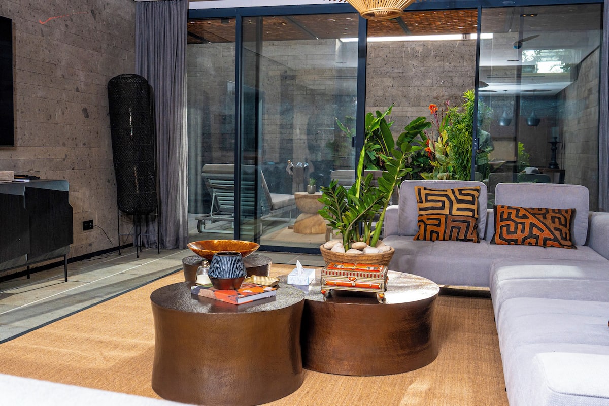 Ein modernes Wohnzimmer mit einer Couch, zwei runden Couchtischen und einem großen Fenster mit Blick ins Freie.