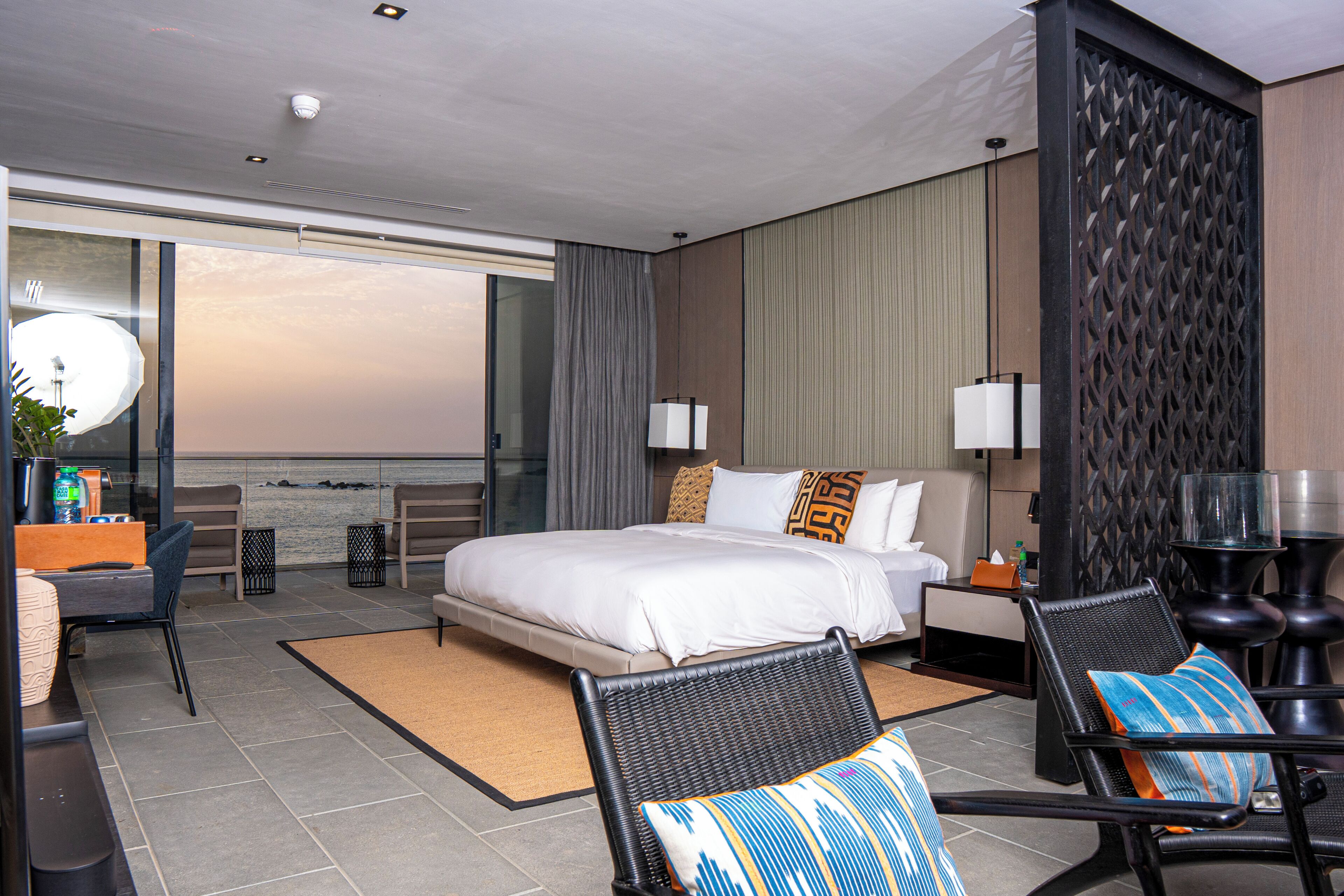A hotel room with a large bed, two chairs, a desk, and a view of the sky.
