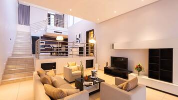 A modern living room with a staircase, a flat-screen TV, and a dining area.