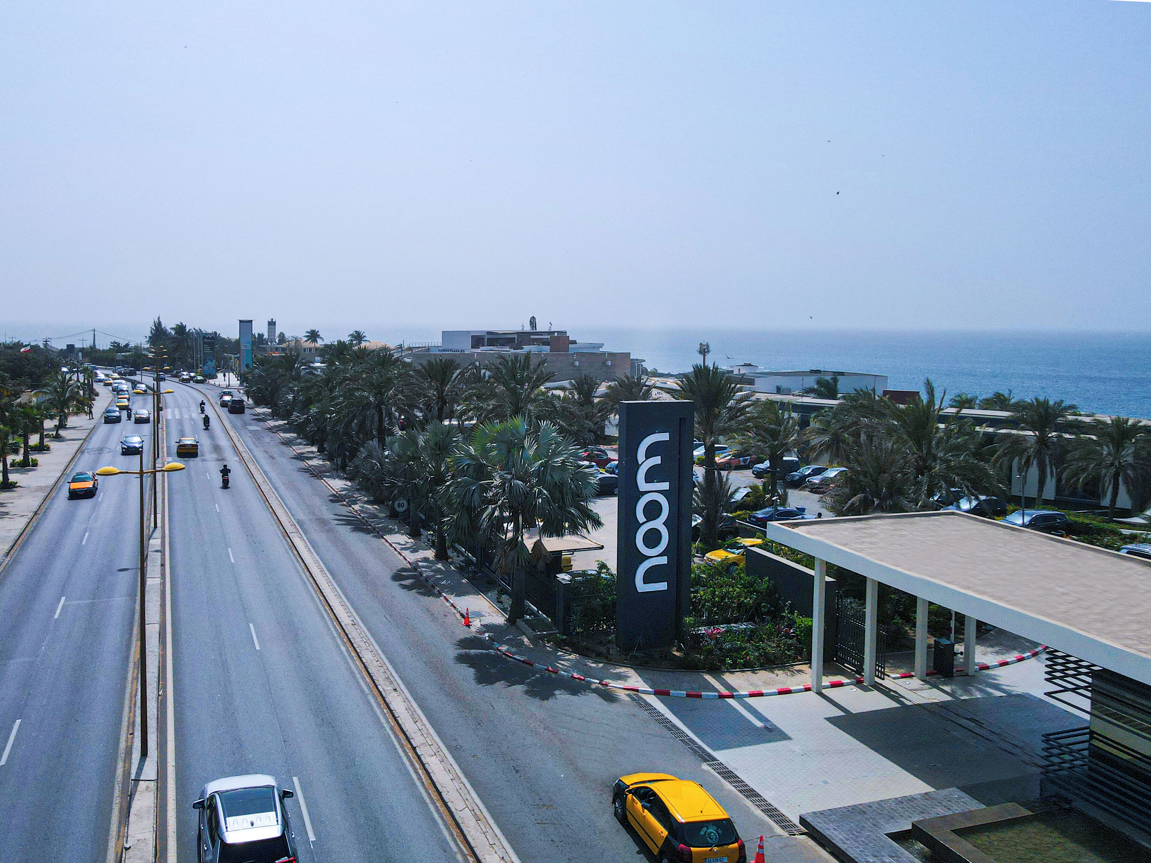 A coastal road with a hotel sign, palm trees, and a view of the sea.