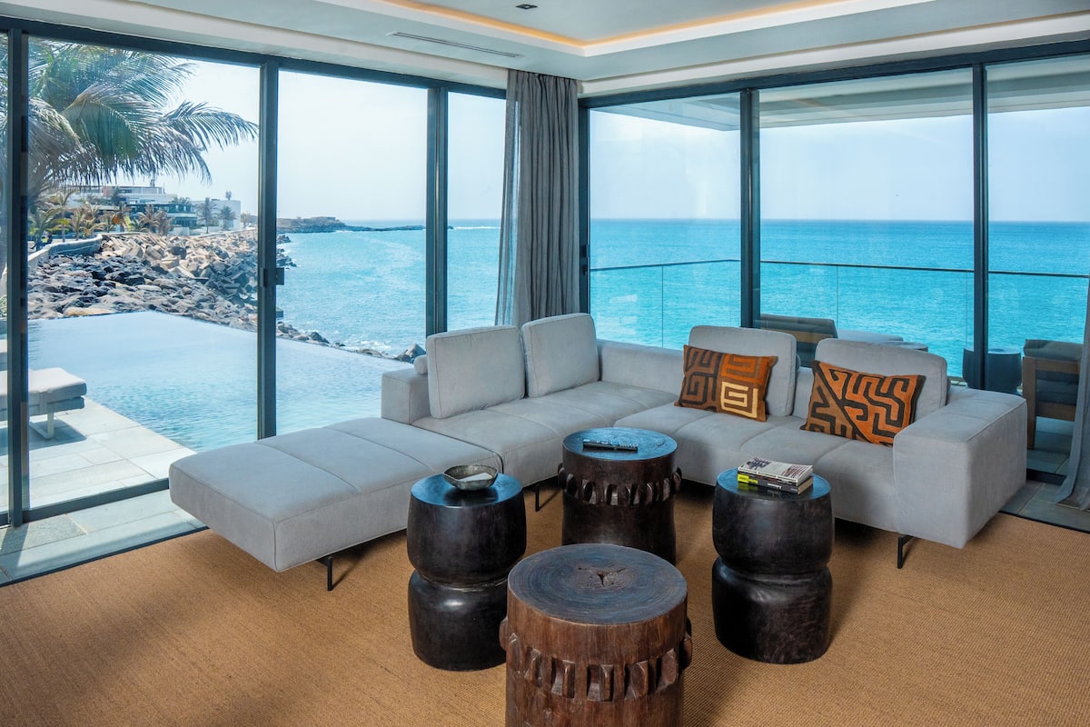 Ein modernes Wohnzimmer mit einer großen Couch, Holztischen und Blick auf den Ozean.
