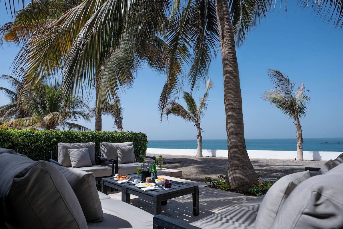 Eine Strandlounge mit Sitzgelegenheiten im Freien, einem Esstisch mit Speisen und Getränken sowie Blick auf den Ozean.