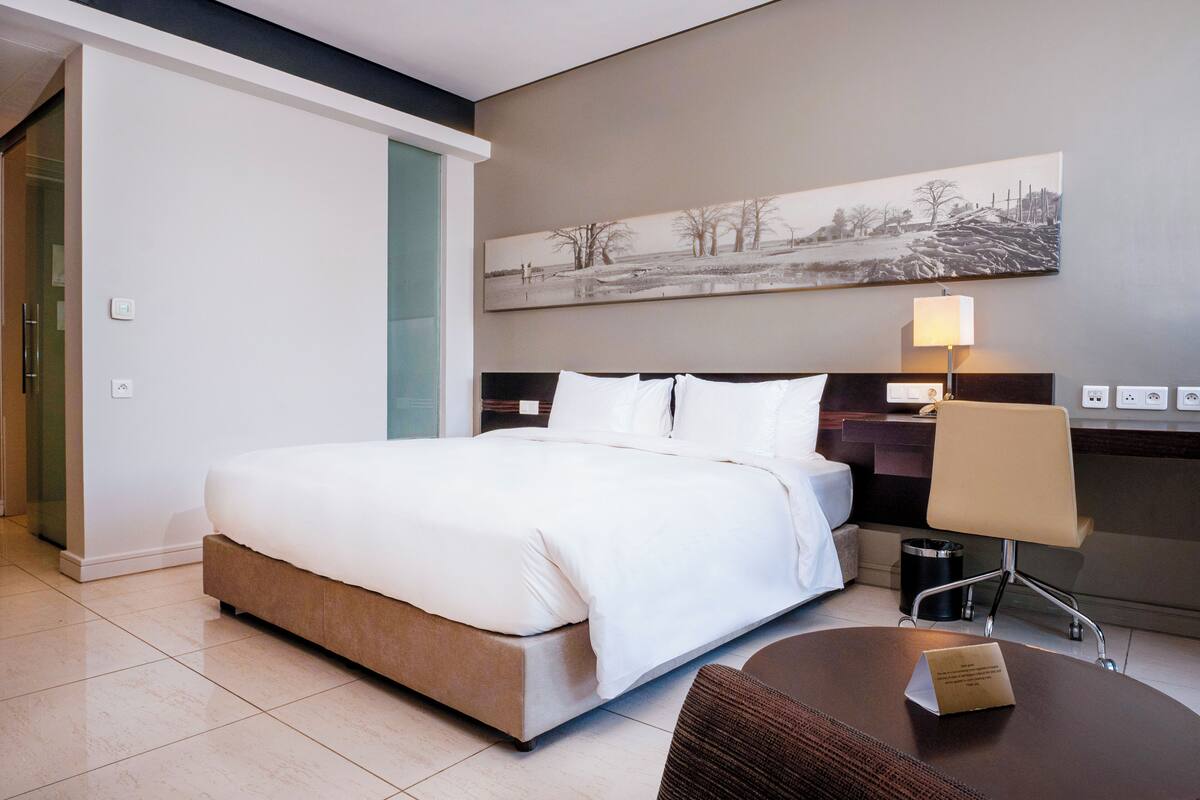 Ein Hotelzimmer mit einem großen Bett, einem Schreibtisch mit Stuhl, einer Lampe und einem Gemälde an der Wand.