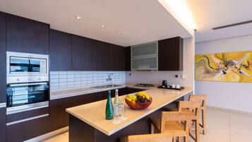 Una cocina moderna con armarios oscuros, horno empotrado, un lavamanos y una isla central con un cuenco de fruta y botellas.
