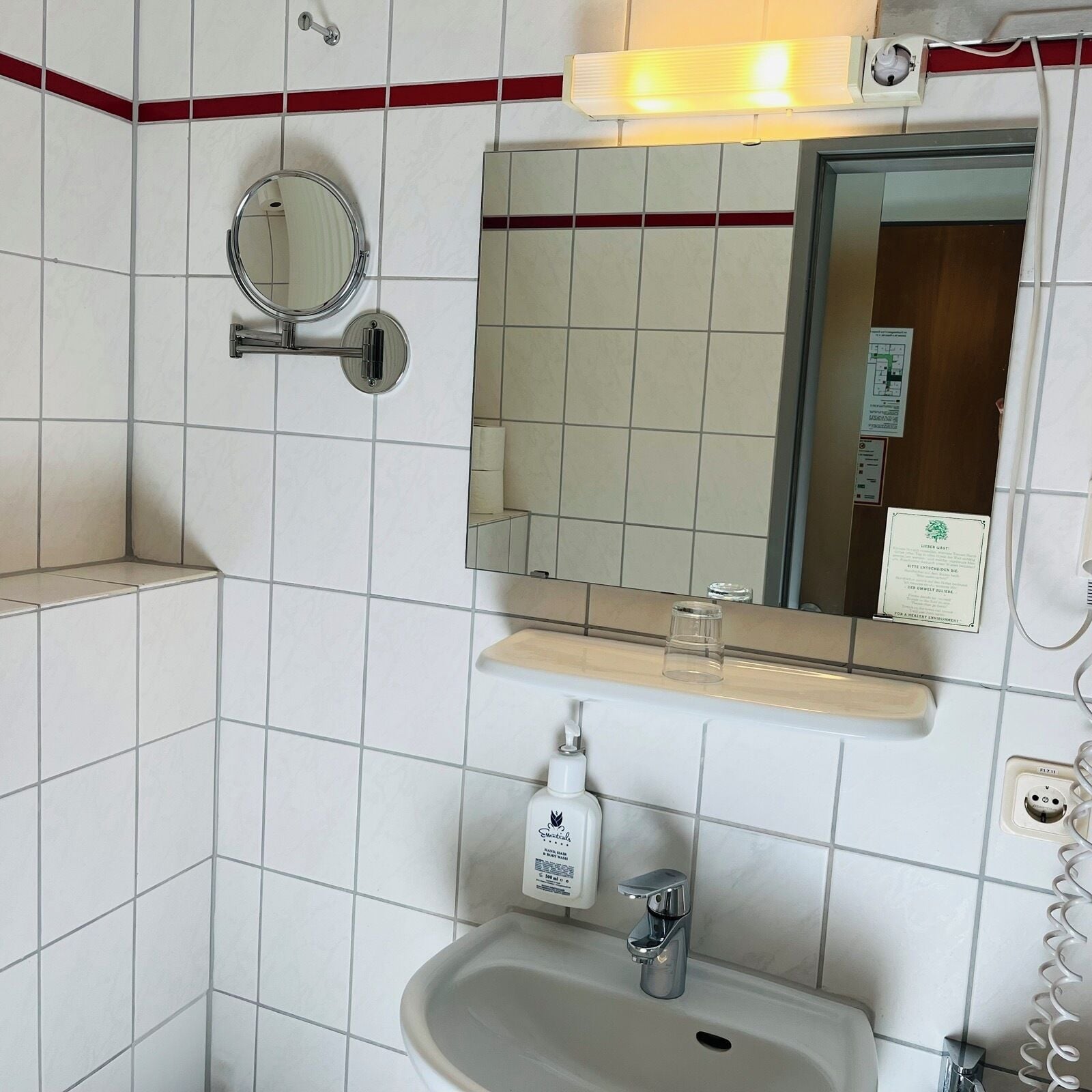 Et badeværelse med en hvid vask, et spejl, en sæbedispenser og en håndklædestang.