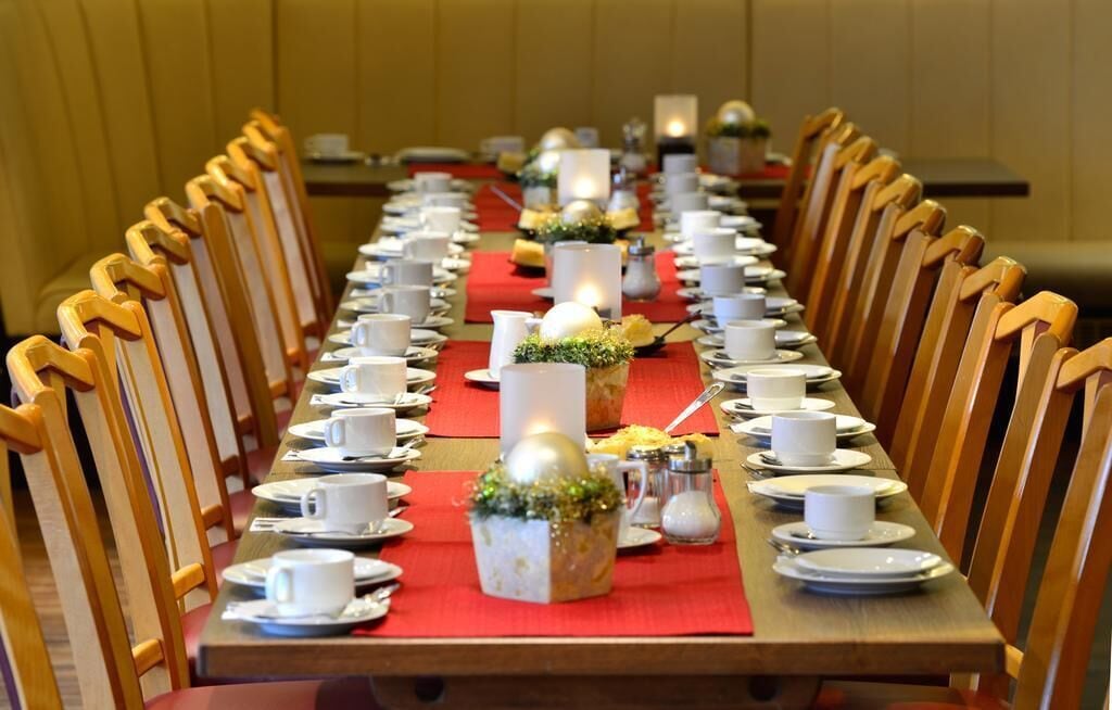 A long dining table with chairs on both sides, set with white cups, saucers, and plates, and decorated with candles and small floral arrangements.