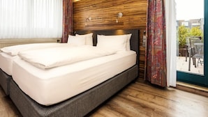 A hotel room with a large bed, wooden headboard, and a view of the outdoors through a glass door. - Hotel Hansen (Bergisch Gladbach)