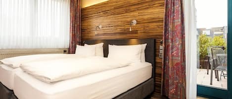A hotel room with a large bed, wooden headboard, and a view of the outdoors through a glass door.