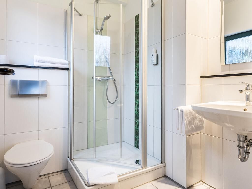 Un bagno moderno con doccia vetrata, un water bianco e un lavandino con specchio sopra.