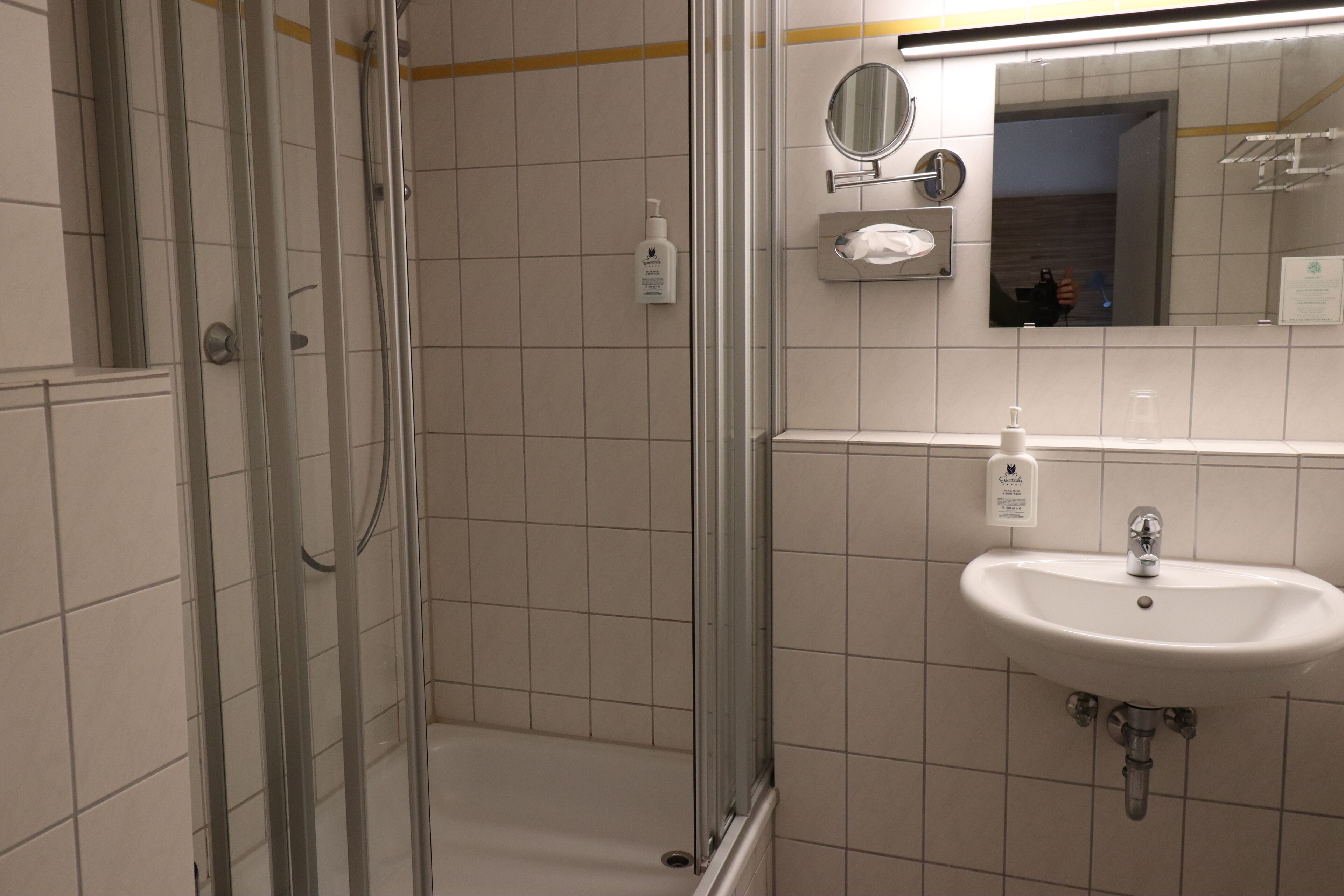 Un baño con cabina de ducha de vidrio, lavabo con espejo y dispensador de jabón.