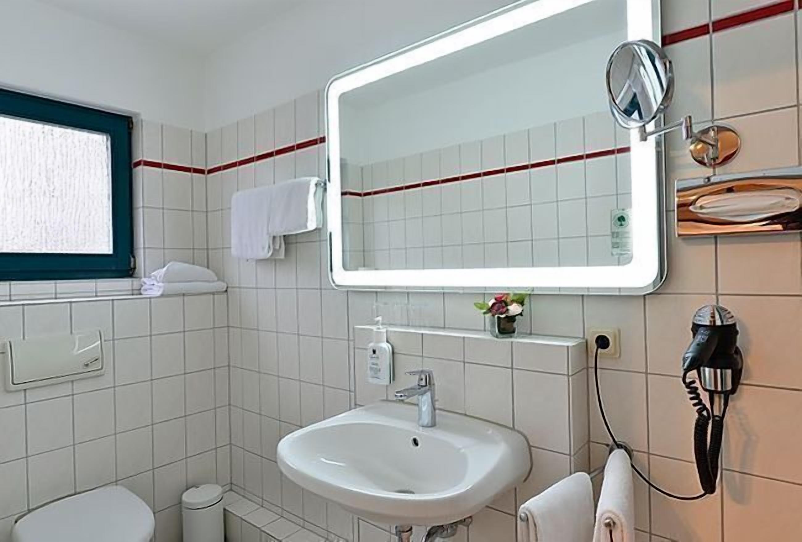 A bathroom with a white sink, a mirror, a towel rack, and a window.