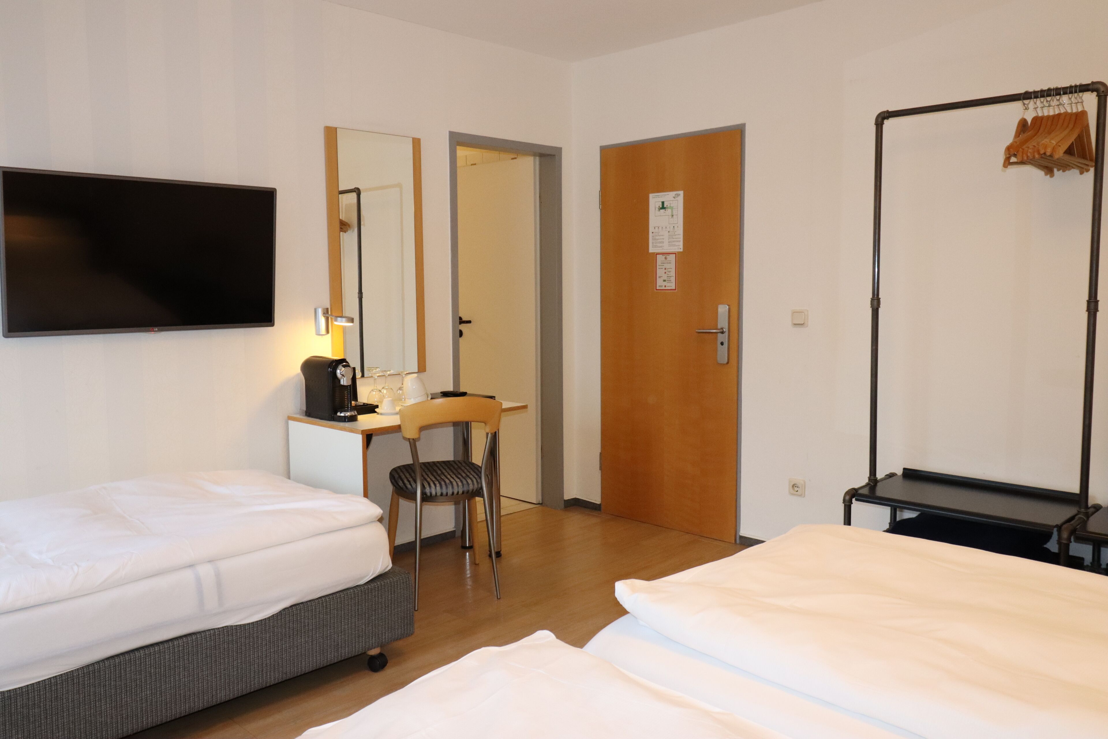 Habitación de hotel con dos camas, un escritorio con silla, televisor y armario con un tendedero.