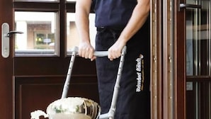 A person in a dark blue shirt and apron pushing a cart with a large white bowl and a sign that reads "CLEAN UP". - Hotel Hansen (Bergisch Gladbach)