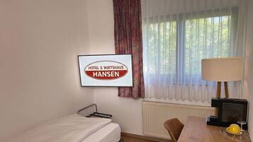 Ein Hotelzimmer mit Bett, Schreibtisch mit Lampe, Fernseher und einem fenster mit Vorhängen.