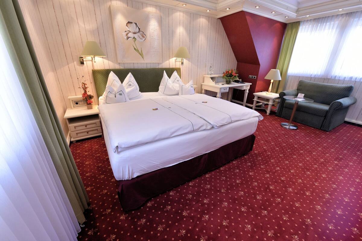 A hotel room with a large bed, a desk, a chair, and a painting on the wall.