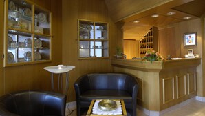 Een houten interieur met een receptiebalie, twee leren stoelen, en een presentatie van klokken en keramiek.