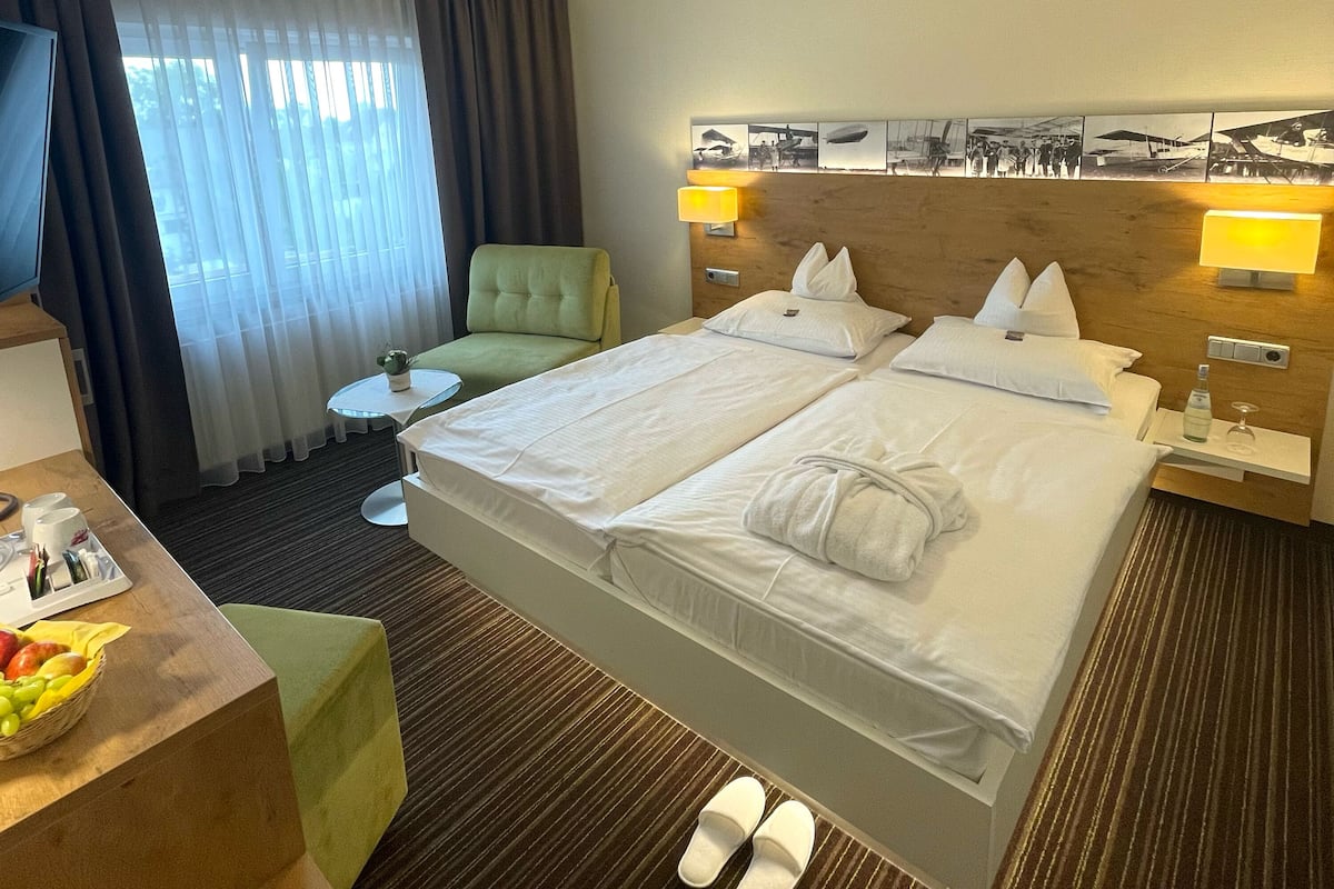 Une chambre d’hôtel avec deux lits, un bureau avec une chaise, une petite table et un téléviseur.