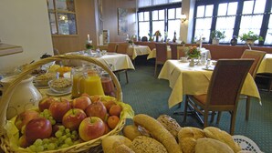 Een ontbijtruimte met gedekte tafels, met fruit, brood en drankjes.