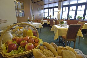 A dining area with tables set for breakfast, featuring fruits, bread, and beverages.