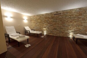A spa room with stone walls, wooden flooring, and two lounge chairs.