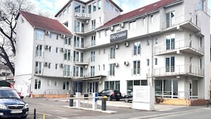 Um hotel com vários andares, varandas, uma placa com a inscrição 'City Center' e um estacionamento com carros.
