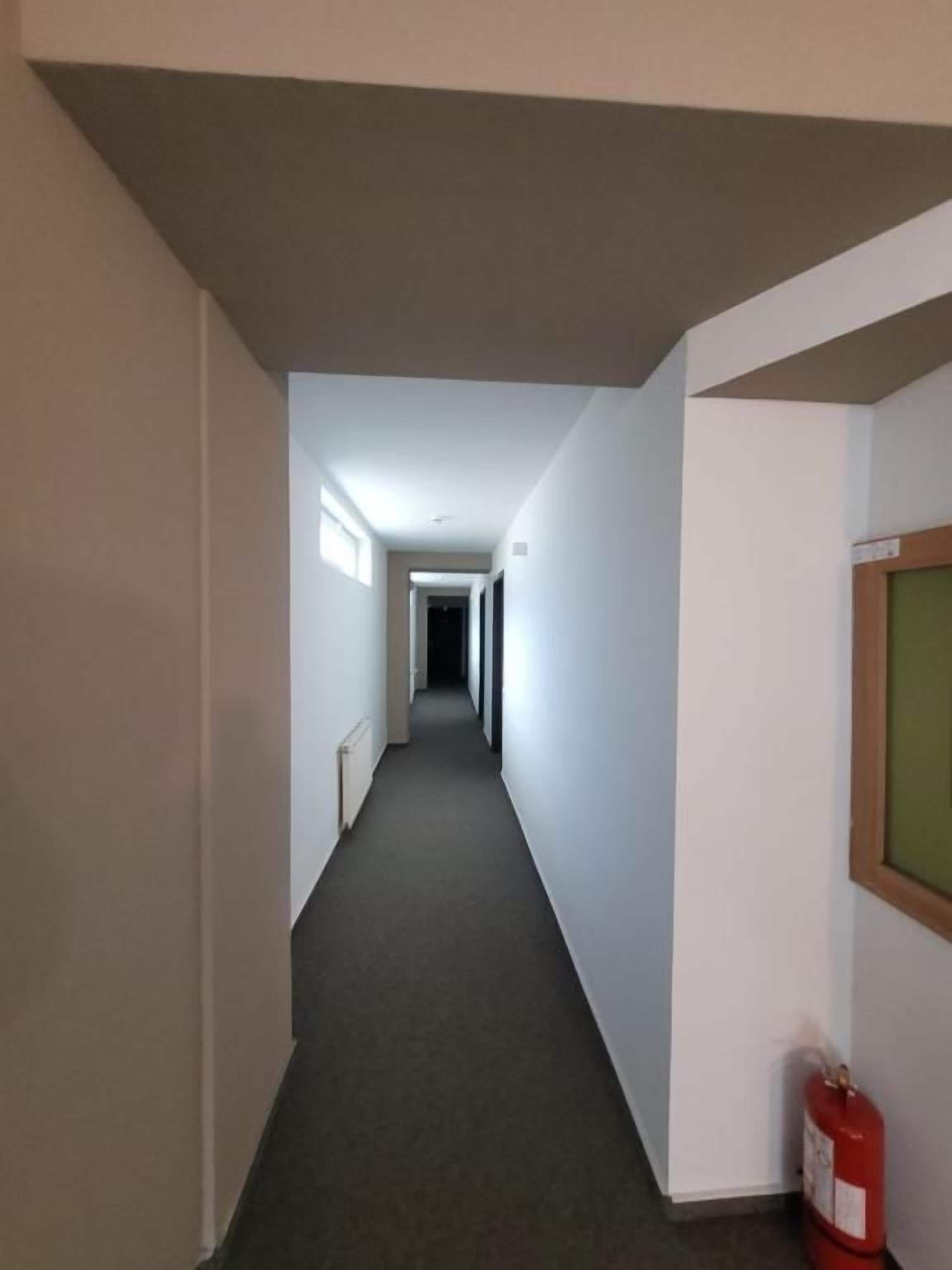 Un pasillo estrecho con piso alfombrado, paredes blancas y un extintor de incendios montado en la pared derecha.