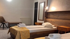 Quarto de hotel com duas camas, um painel de cabeceira de madeira, um espelho, um radiador e uma cadeira.