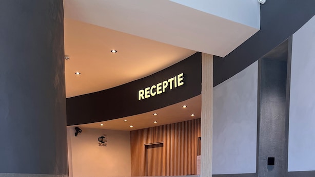 Uma área de recepção com uma placa indicando 'RECEPTION', um balcão de madeira e piso de azulejos.