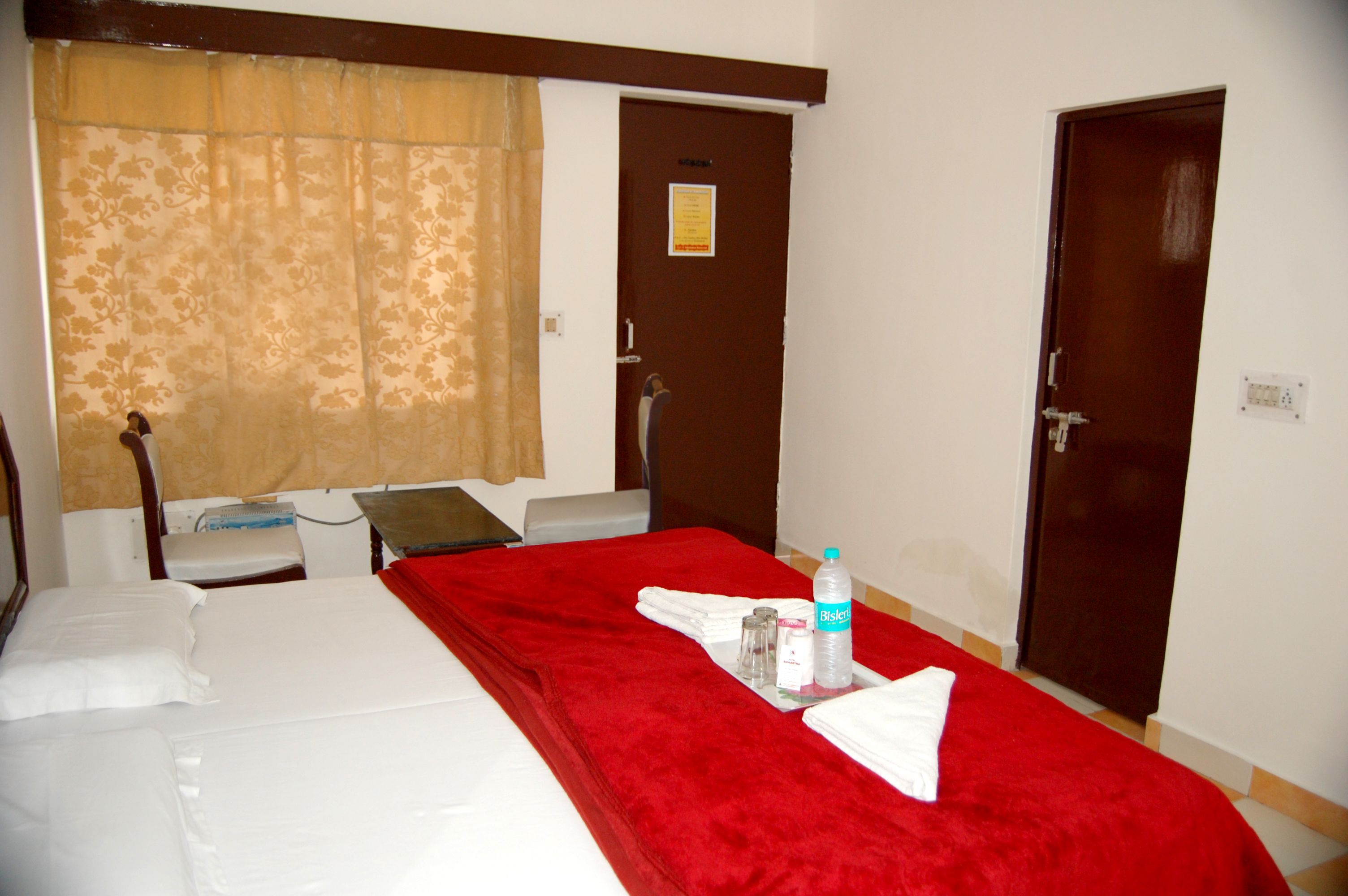 A hotel room with a bed, a red blanket, a bottle of water, and a set of towels.