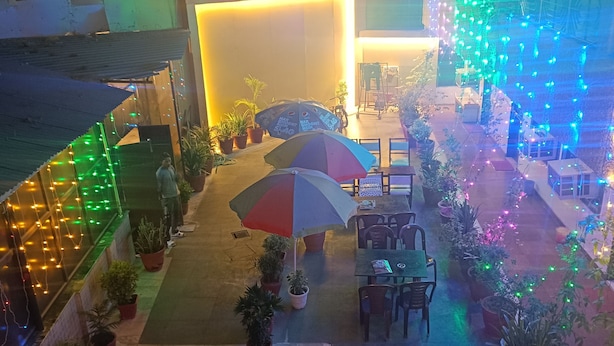 An outdoor seating area with tables and chairs, surrounded by potted plants and illuminated by string lights. - Hotel Sidhartha (Agra)