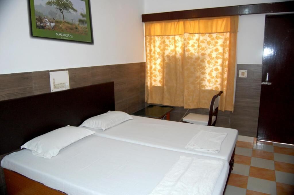 A double bed with white linens, a wooden headboard, a small table with a chair, and a door with a wooden frame.