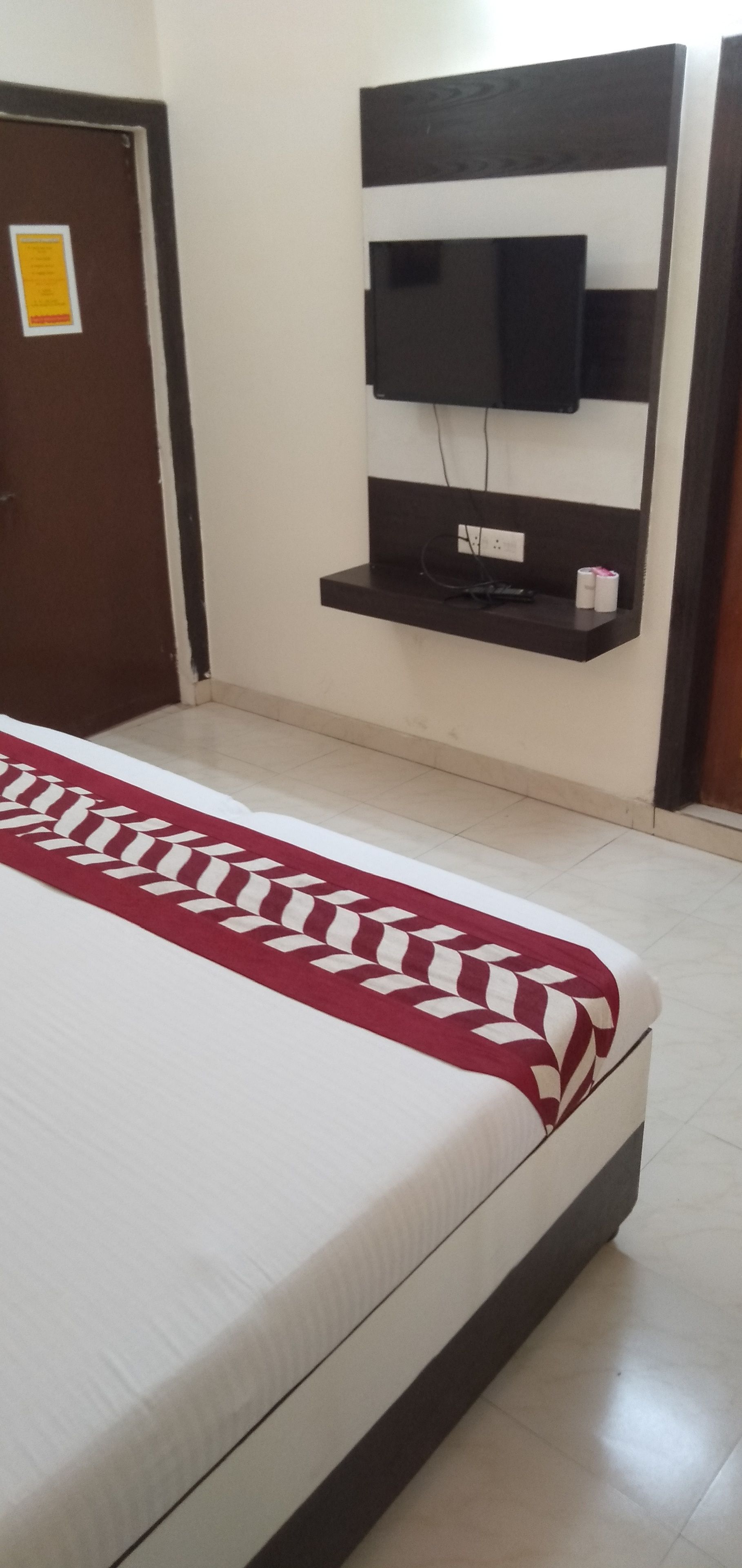 Una cama con una colcha estampada, un televisor montado y un pequeño estante con un control remoto.
