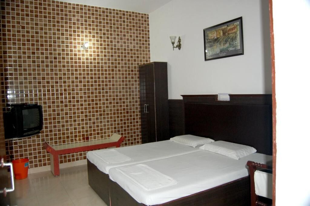 Una habitación de hotel con una cama, un televisor, un banco rojo y una pared de azulejos.