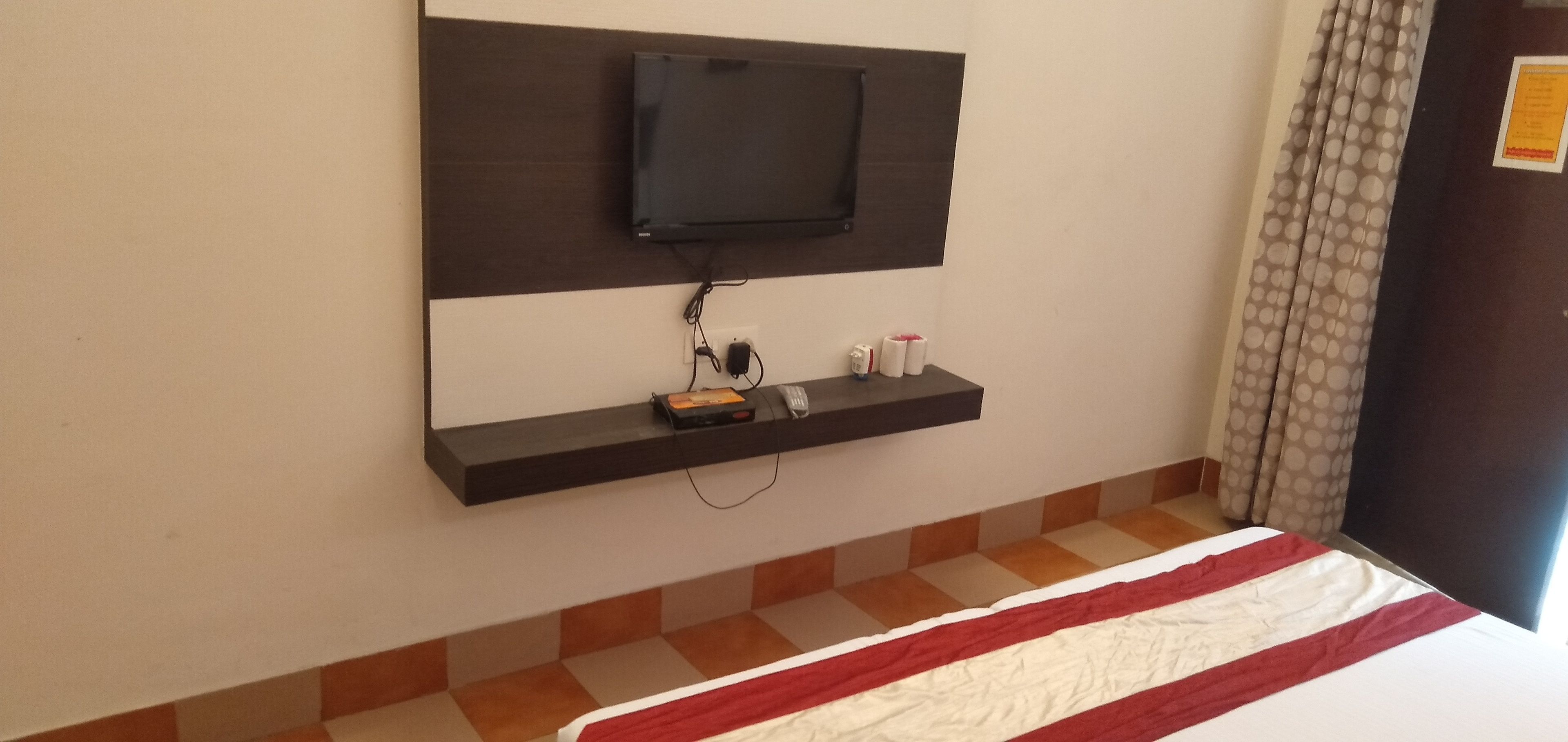 Habitación de hotel con televisor de pantalla plana montado en la pared, repisa con artículos de aseo y cama con colcha a rayas.